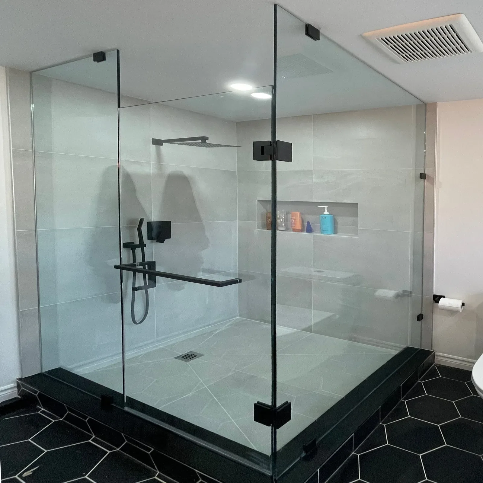 Frameless corner shower enclosure with black hardware over black hexagon floor tile
