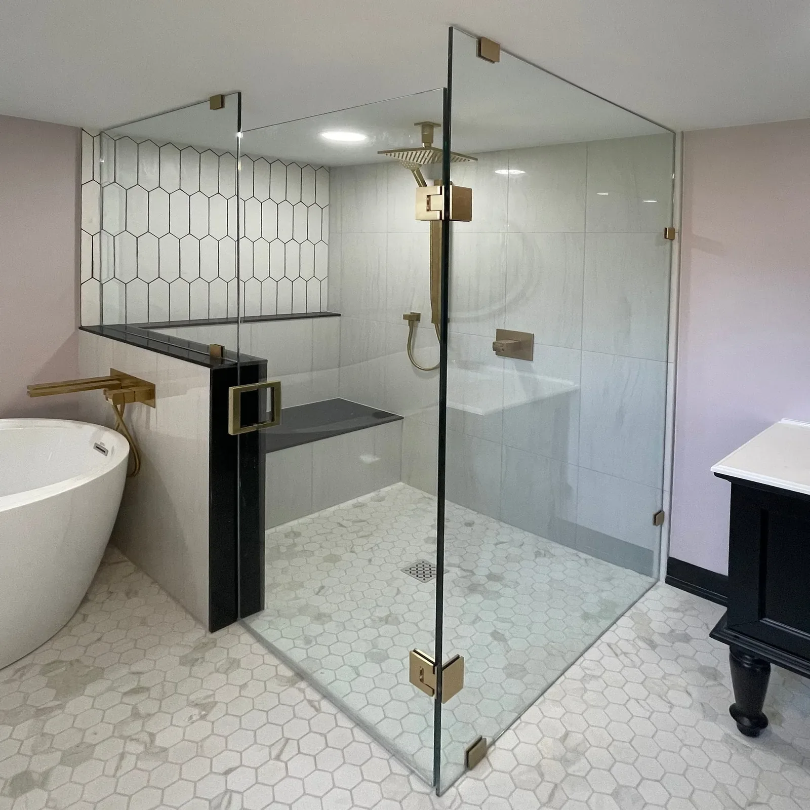 Frameless glass corner shower with brass hardware beside a freestanding tub