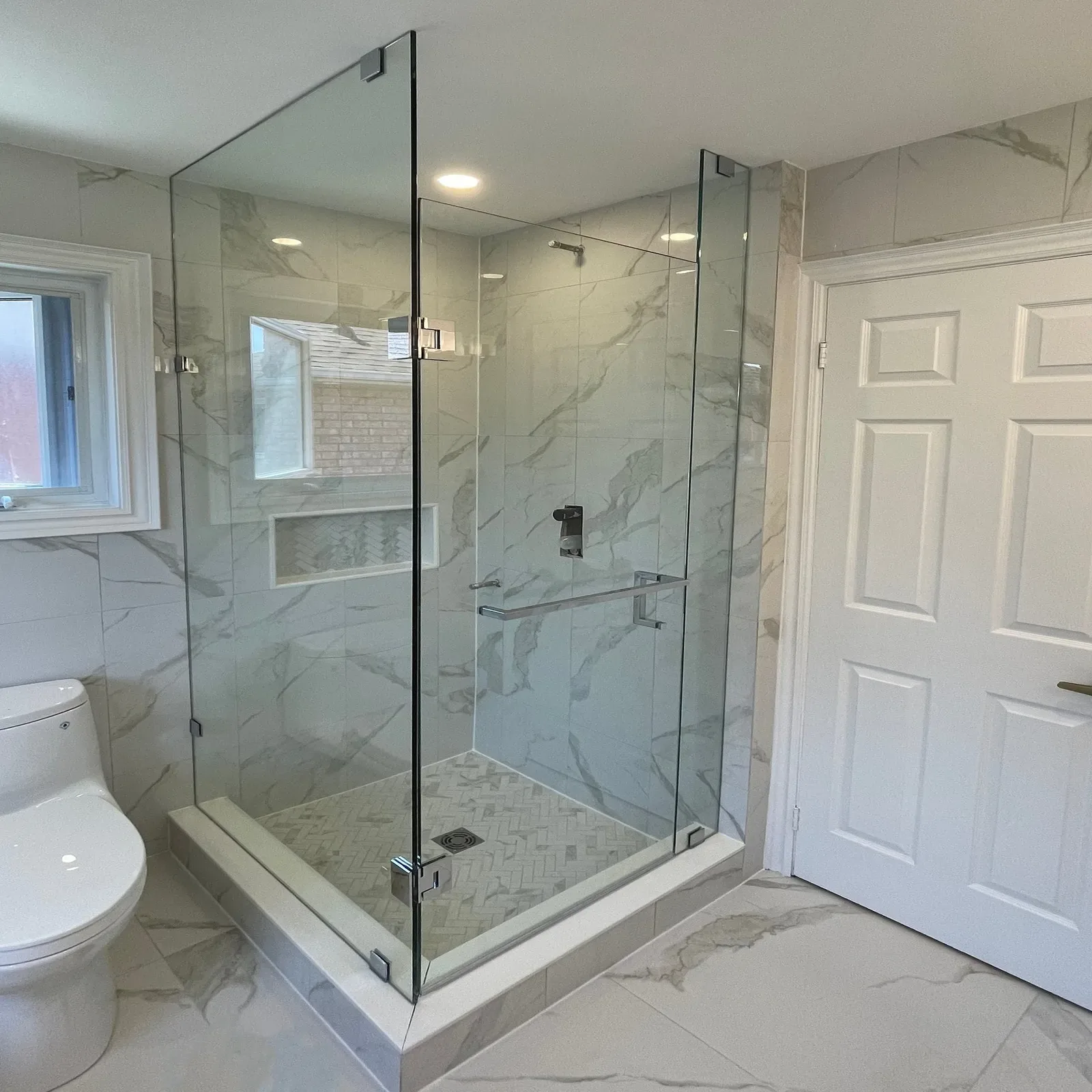 Frameless glass corner shower with a polished chrome towel bar and marble-look walls