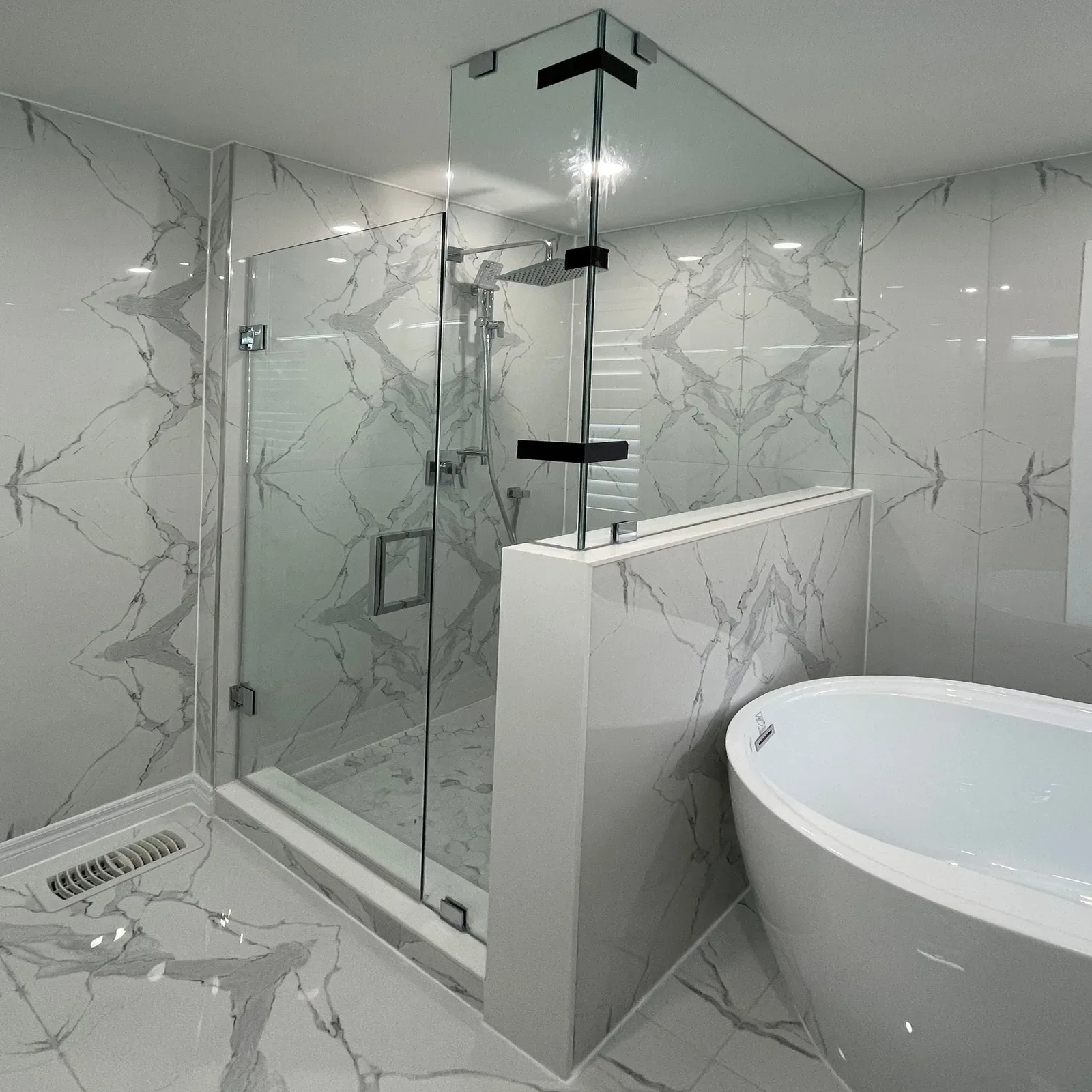 Frameless glass shower with a hinged door and half-wall panel beside a freestanding tub