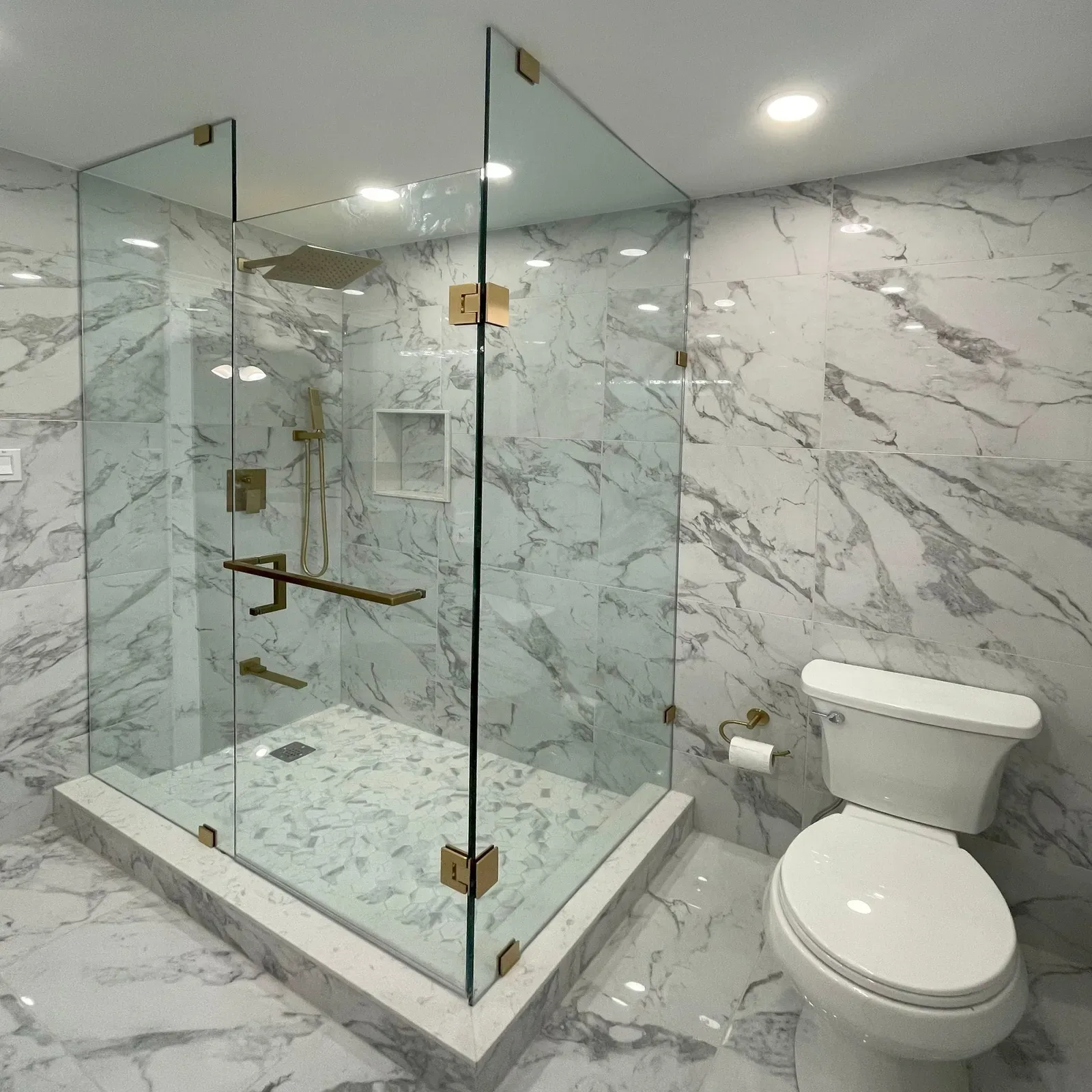 Frameless glass shower with brushed brass hardware and marble tile