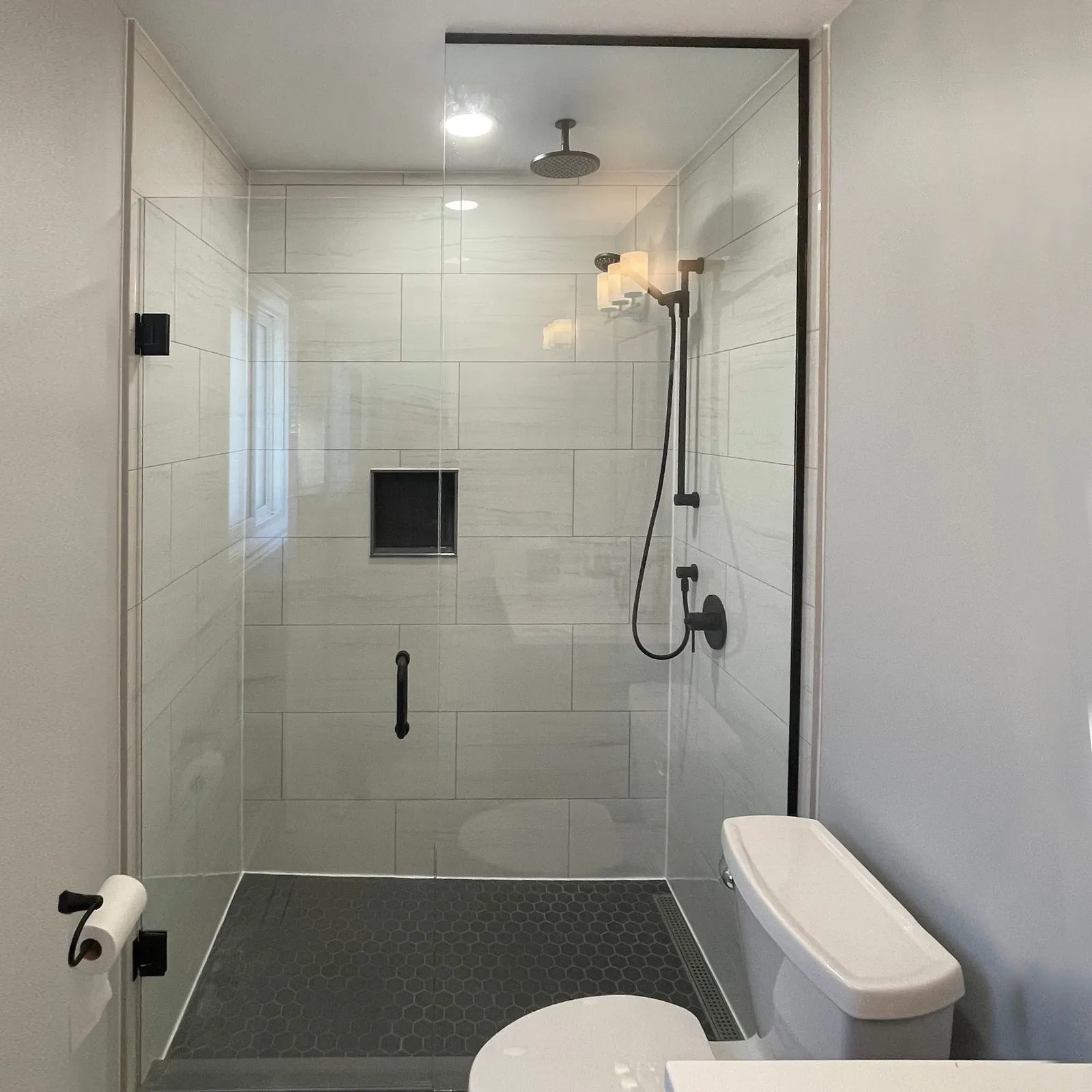 Frameless hinged shower door with black hardware and a black hexagon floor