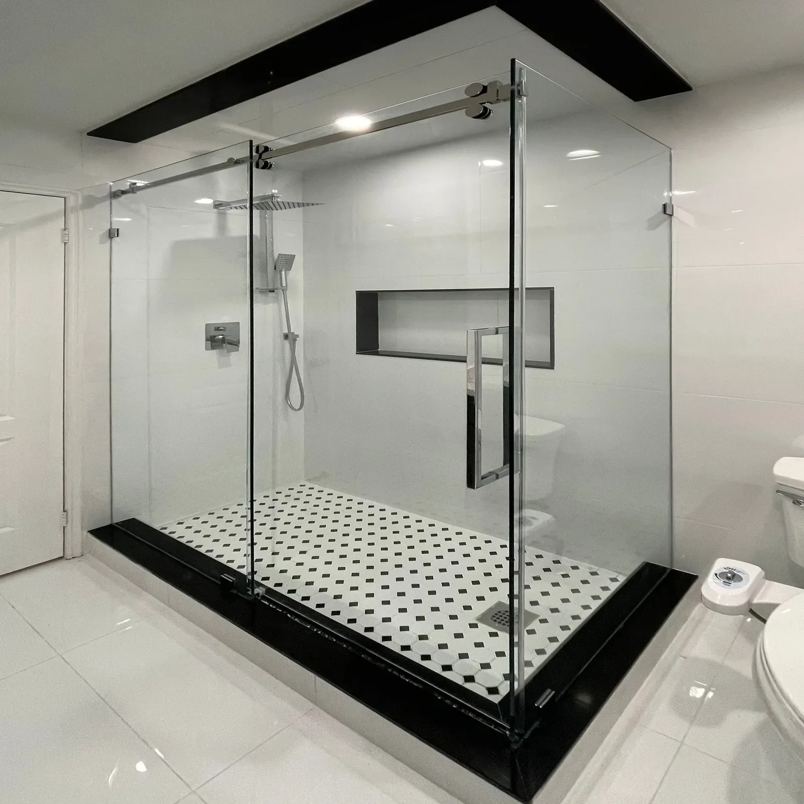 Frameless sliding shower enclosure with a black header beam and black-and-white floor tile